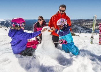 Family building a snowman at Perisher Ski Village in the Snowy Mountains after a day of skiing.
