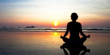 Silhouette yoga woman sitting on sea coast at sunset.